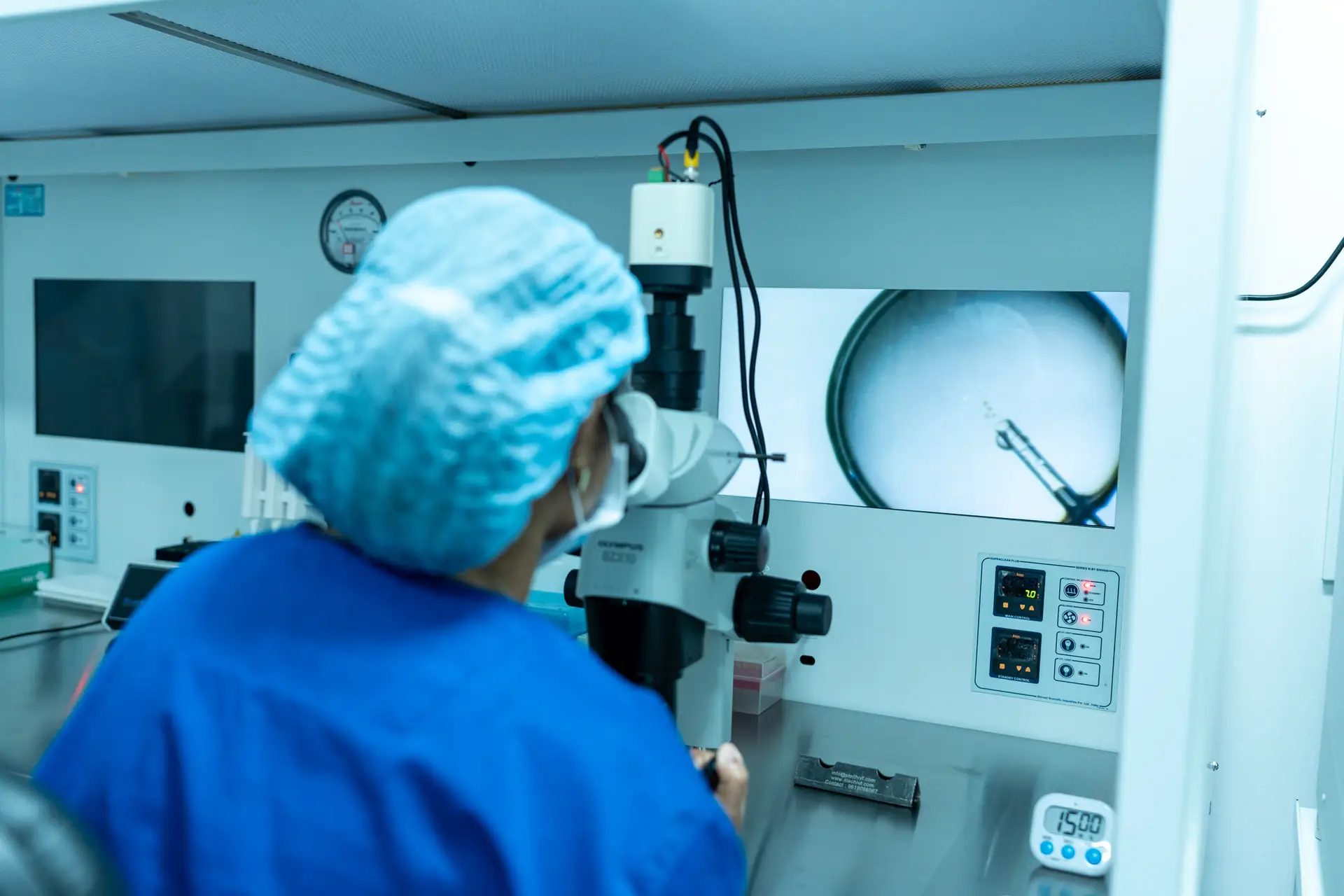Embryologist observing a laboratory procedure through a microscope with magnified imaging displayed on screen at Khushi Fertility & IVF Centre, Bengaluru.